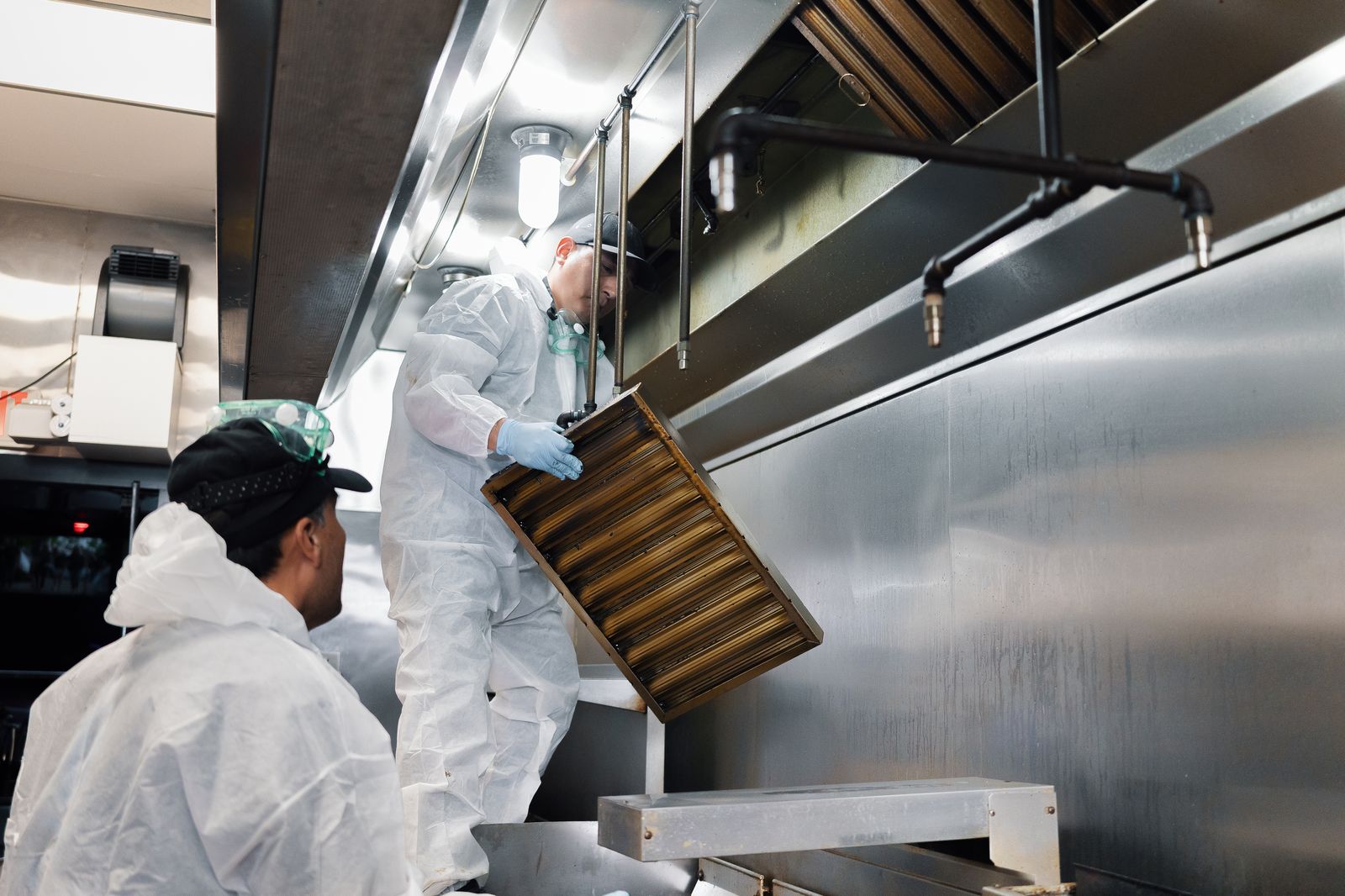 TruShine technicians removing grease baffle filters from commercial kitchen exhaust hood for cleaning