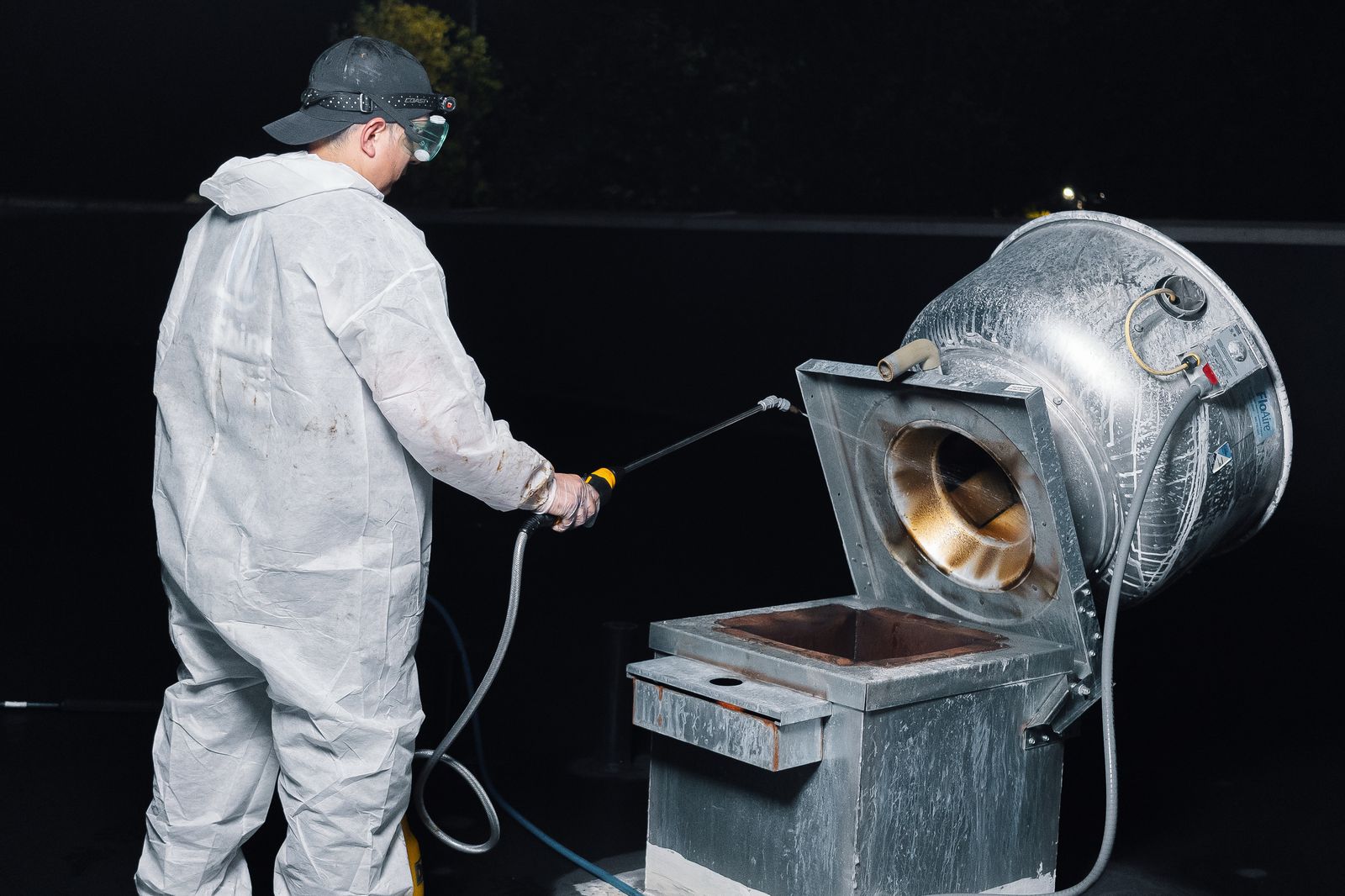 TruShine technician cleaning commercial kitchen exhaust fan on rooftop at night in Atlanta with headlamp and pressure washer