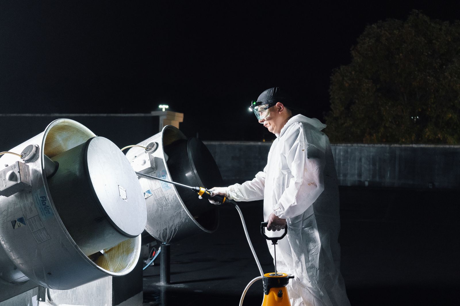 TruShine technician pressure washing commercial exhaust fan on restaurant rooftop at night with headlamp illuminating the work